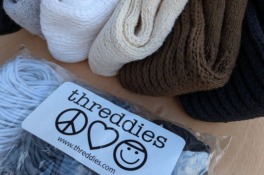 a pile of threddies cotton slouch socks, next to a package of threddies elastic hair ties